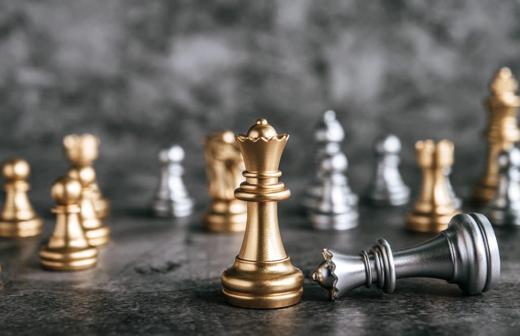 Close-up of a gold king chess piece in focus on a dark chessboard, with other pieces blurred in the background.