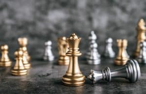 Close-up of a gold king chess piece in focus on a dark chessboard, with other pieces blurred in the background.