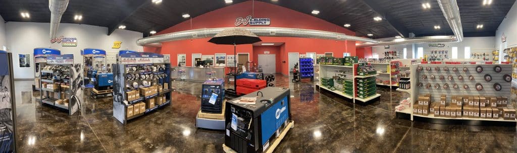 Welding supply store interior with display racks, welding machines, and red back wall in a spacious showroom.