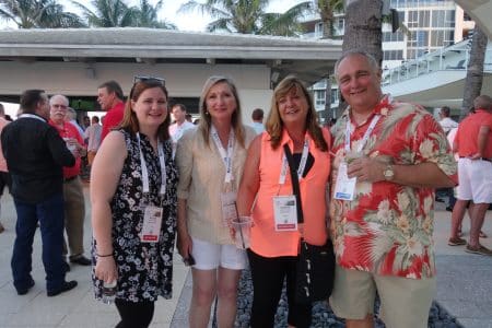 Four adults posing for a group photo at an outdoor event, wearing name badges and lanyards.