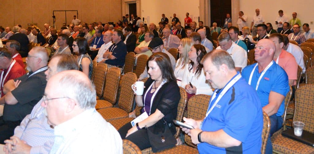 Large crowd seated in a conference hall listening to a presentation at a daytime event.