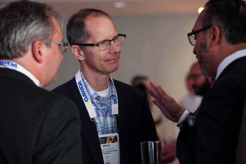 Man in glasses with a conference badge talking with two colleagues at a networking event.