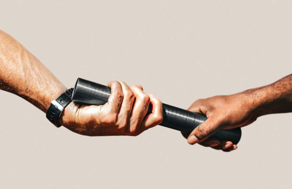Two hands pass a black baton during a relay race, close up of the exchange between runners.