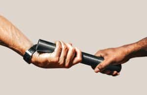Two hands pass a black baton during a relay race, close up of the exchange between runners.