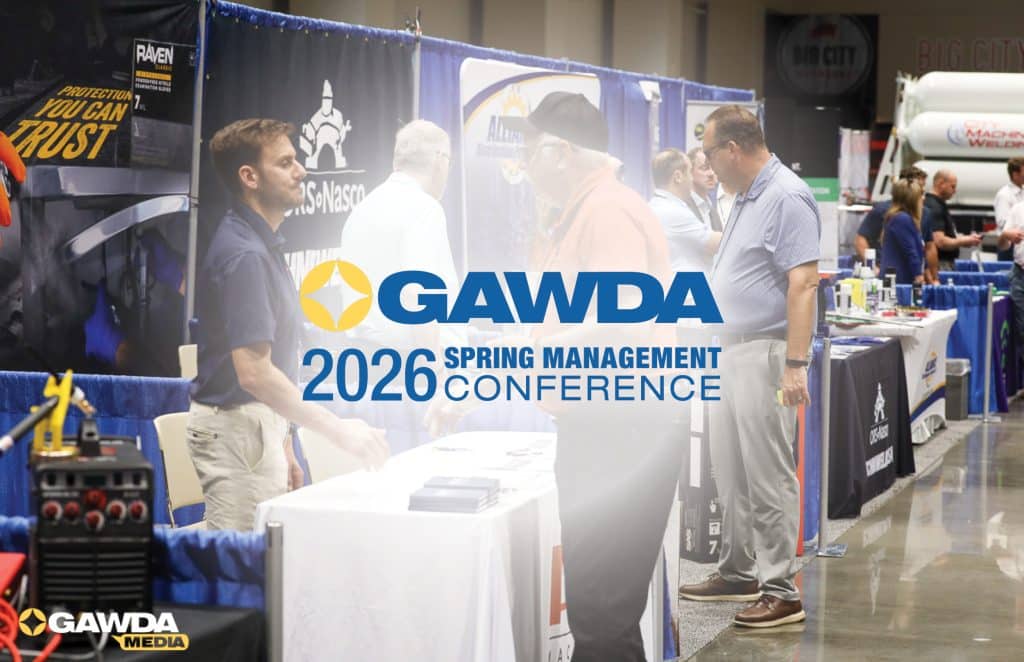 Exhibition hall at a conference with GAWDA branding and attendees talking at booth tables with blue dividers.