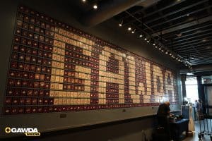 Wall filled with hundreds of small red-and-white square icons; GAWDA MEDIA logo bottom left; man at a reception desk on the right.