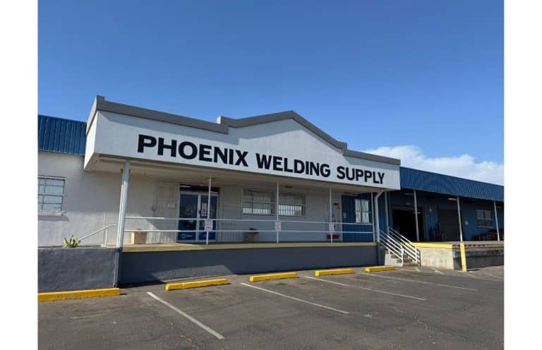 Front of Phoenix Welding Supply storefront with a large black sign, white facade, and parking lot under a blue sky.