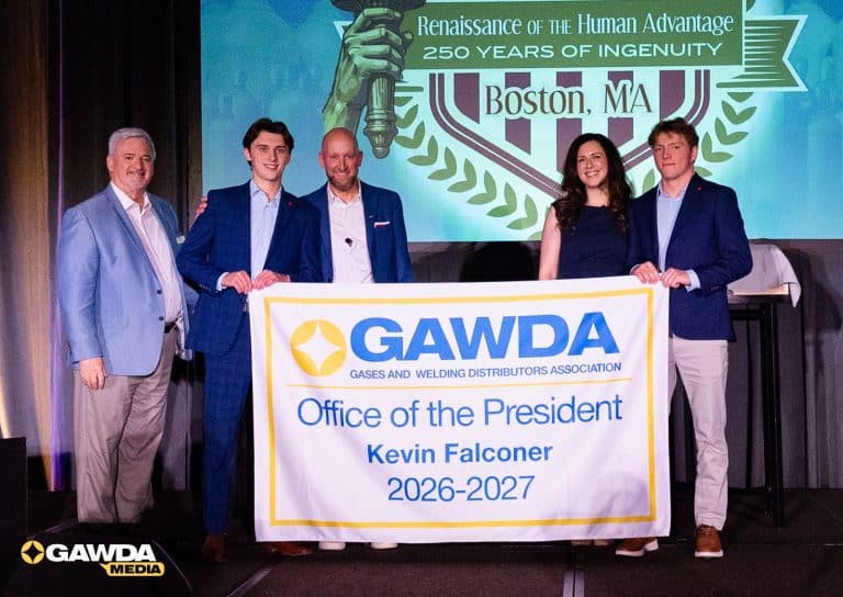 Group of five adults in business attire posing on a stage, holding a banner that reads GAWDA—Office of the President Kevin Falconer 2026–2027, commemorating a leadership event on stage with a backdrop.