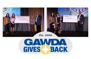Group of recipients on a stage posing with oversized ceremonial checks during a GAWDA Gives Back event, backdrop shows the GAWDA logo.
