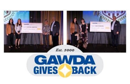 Group of recipients on a stage posing with oversized ceremonial checks during a GAWDA Gives Back event, backdrop shows the GAWDA logo.