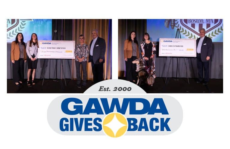 Group of recipients on a stage posing with oversized ceremonial checks during a GAWDA Gives Back event, backdrop shows the GAWDA logo.