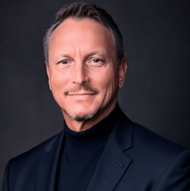 sitemgr_photo_16049 - GAWDA Media Professional headshot of a middle-aged man with short gray hair, wearing a dark turtleneck and navy blazer against a dark backdrop.