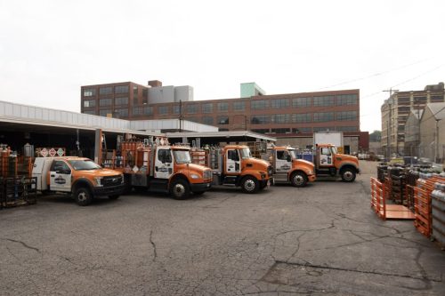 Industrial yard with orange utility trucks parked in front of a red brick warehouse. (Informative)