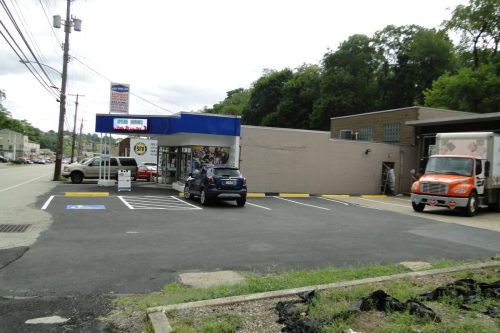 Parking lot in front of a blue storefront with an awning; several cars parked and a large orange truck on the right, with trees behind.