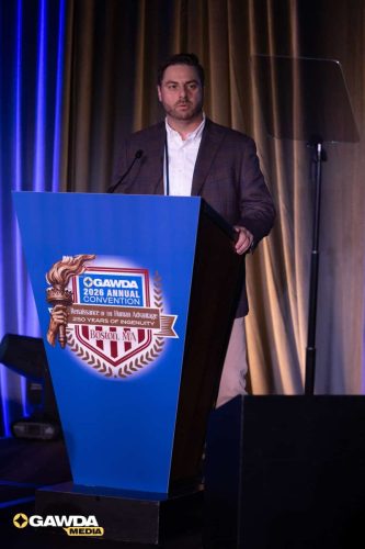 Speaker at the GAWDA 2026 Annual Convention delivering a speech from a blue podium on a stage in Boston, MA.