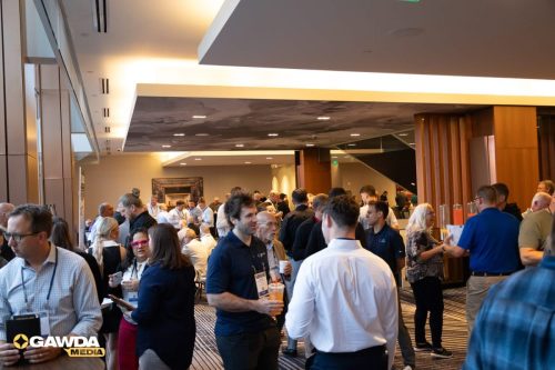 Crowd of professionals networking in a modern conference lobby, many with name badges and drinks in hand.