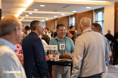 Professionals networking at a high-top table in a conference hall; badge 37 visible and a Red Ball Oxygen sign on the table.