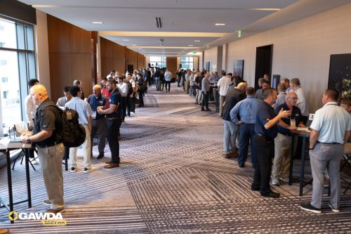 Long conference hallway with attendees networking at tabletop stations along both walls; GAWDA logo visible in the bottom-left corner.