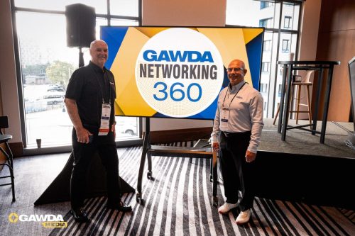Two men stand beside a large display that reads 'GAWDA Networking 360' in a conference room.