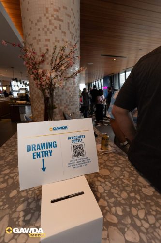 Sign on a countertop announces a drawing entry and newcomer survey with a QR code and a tissue box nearby.