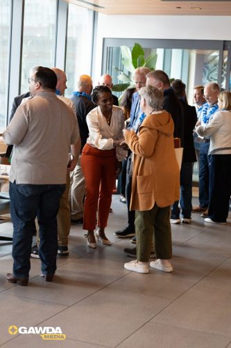 Professionals networking in a bright lobby, with two women shaking hands while others converse nearby.