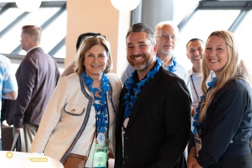 Group of professionals at a conference, smiling for the photo, wearing blue flower leis and name badges.