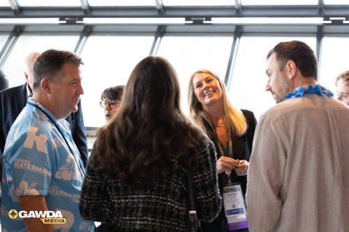 Group of professionals engaged in conversation at a bright conference space, wearing name badges and lanyards. GAWDA Media logo visible in the bottom corner.