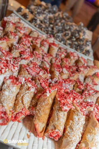Tray of pastry sticks coated with powdered sugar and red candy glaze, arranged in rows for serving.