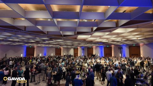 Large conference hall filled with people socializing at a networking event; blue up lighting along the walls.