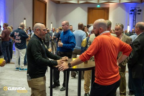 Professionals networking at an indoor reception, standing around a tall round table with drinks in hand.