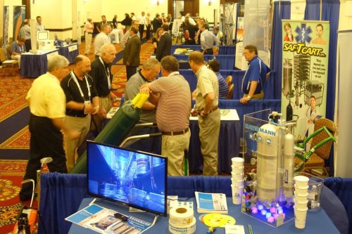 Busy trade show hall with booths, attendees, and medical equipment displays at a convention center.