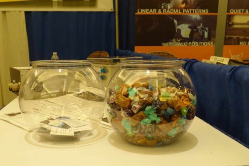 Two glass candy jars on a white table, filled with colorful wrapped candies, with papers scattered nearby and a blue curtain in the background.