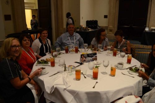 Group of adults seated around a round banquet table in a formal dining room, enjoying salads and drinks during a social event.
