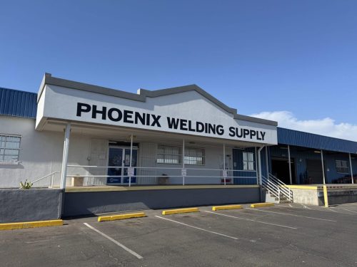 Storefront of Phoenix Welding Supply building with bold black lettering, blue sky, and a parking lot in front.