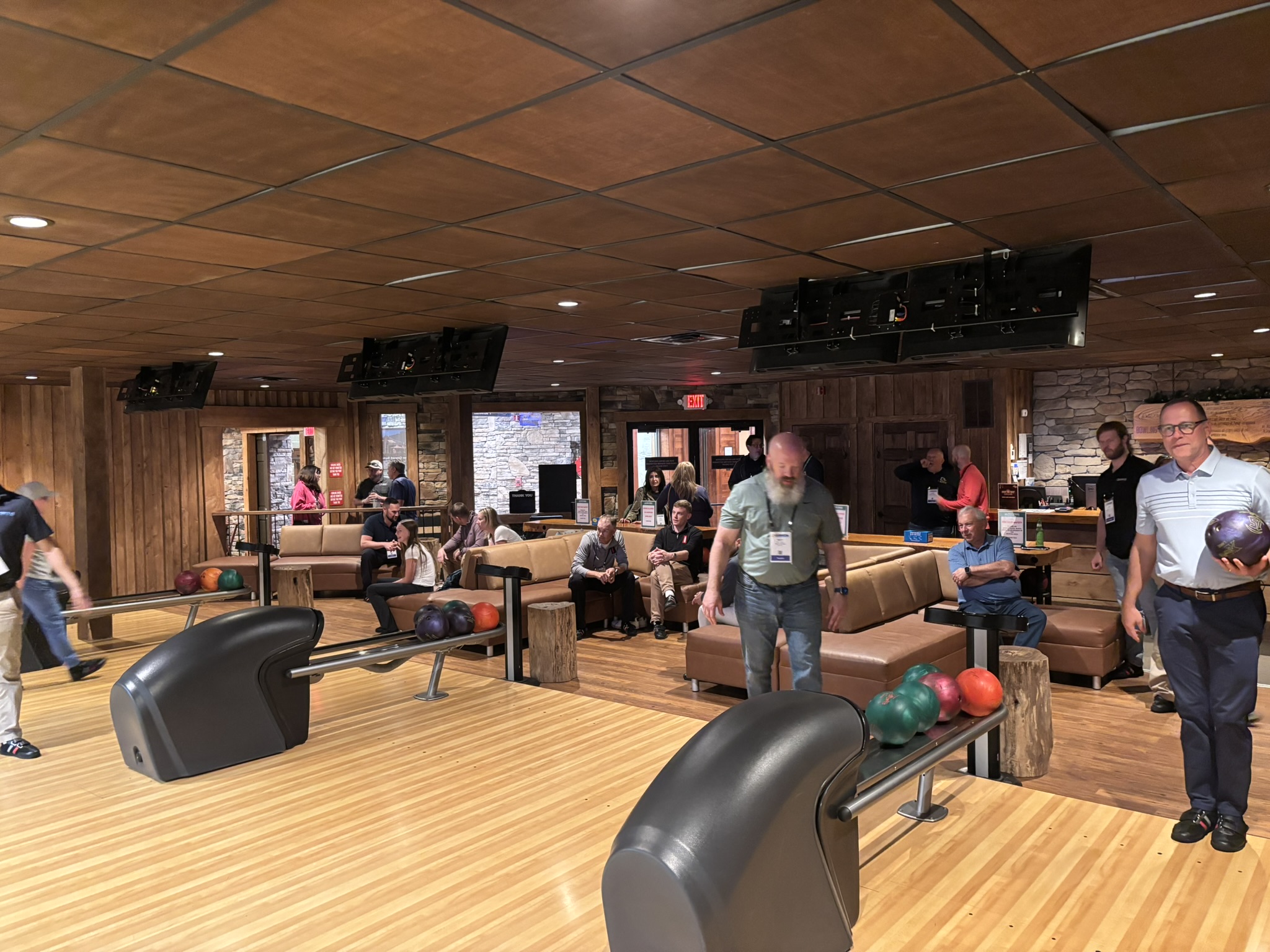 People bowling in a cozy, wood-paneled bowling alley with lanes, balls, and seating areas in the background.