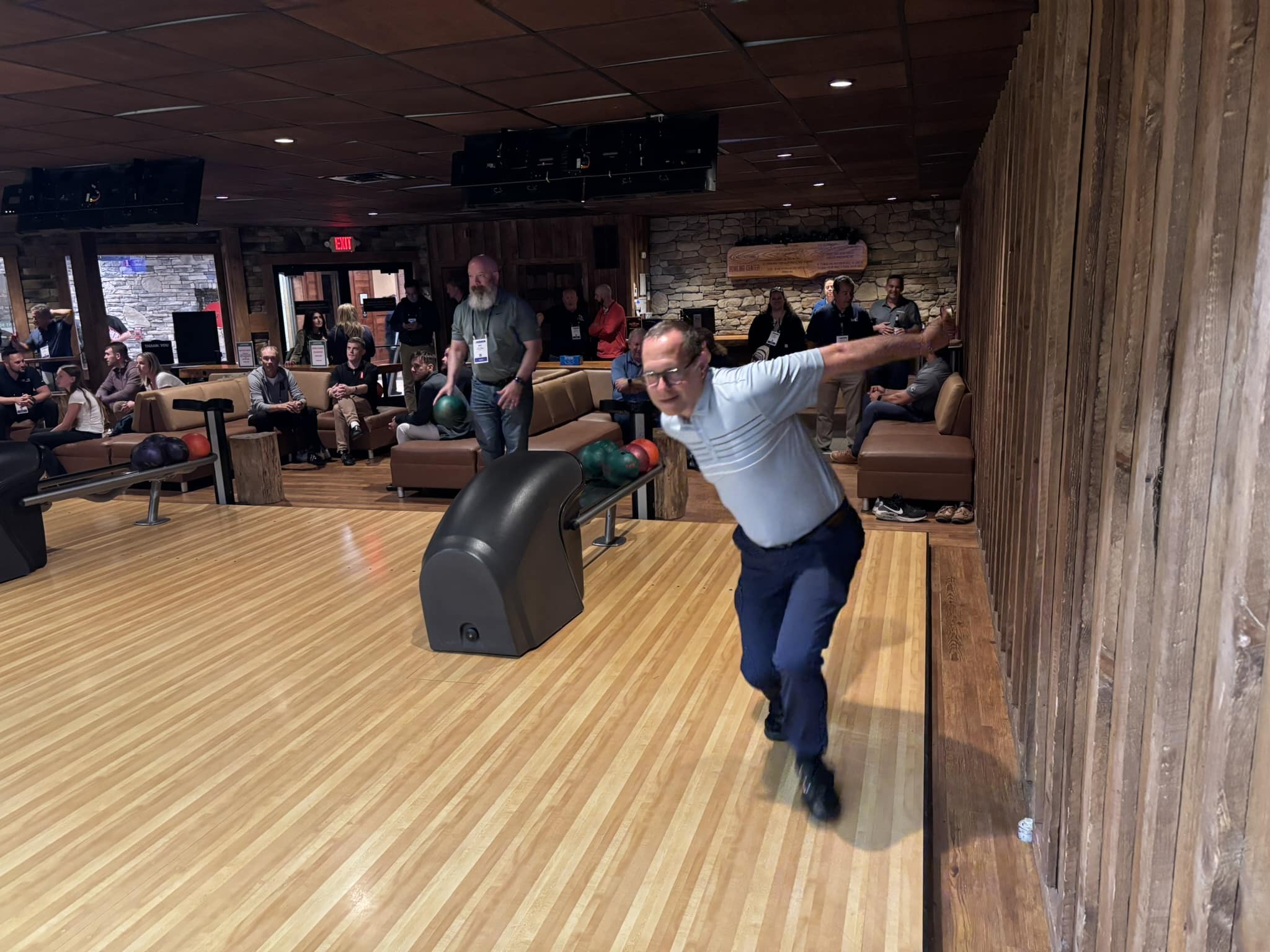 Bowling alley scene with a man mid-throw; spectators sit on couches watching nearby.