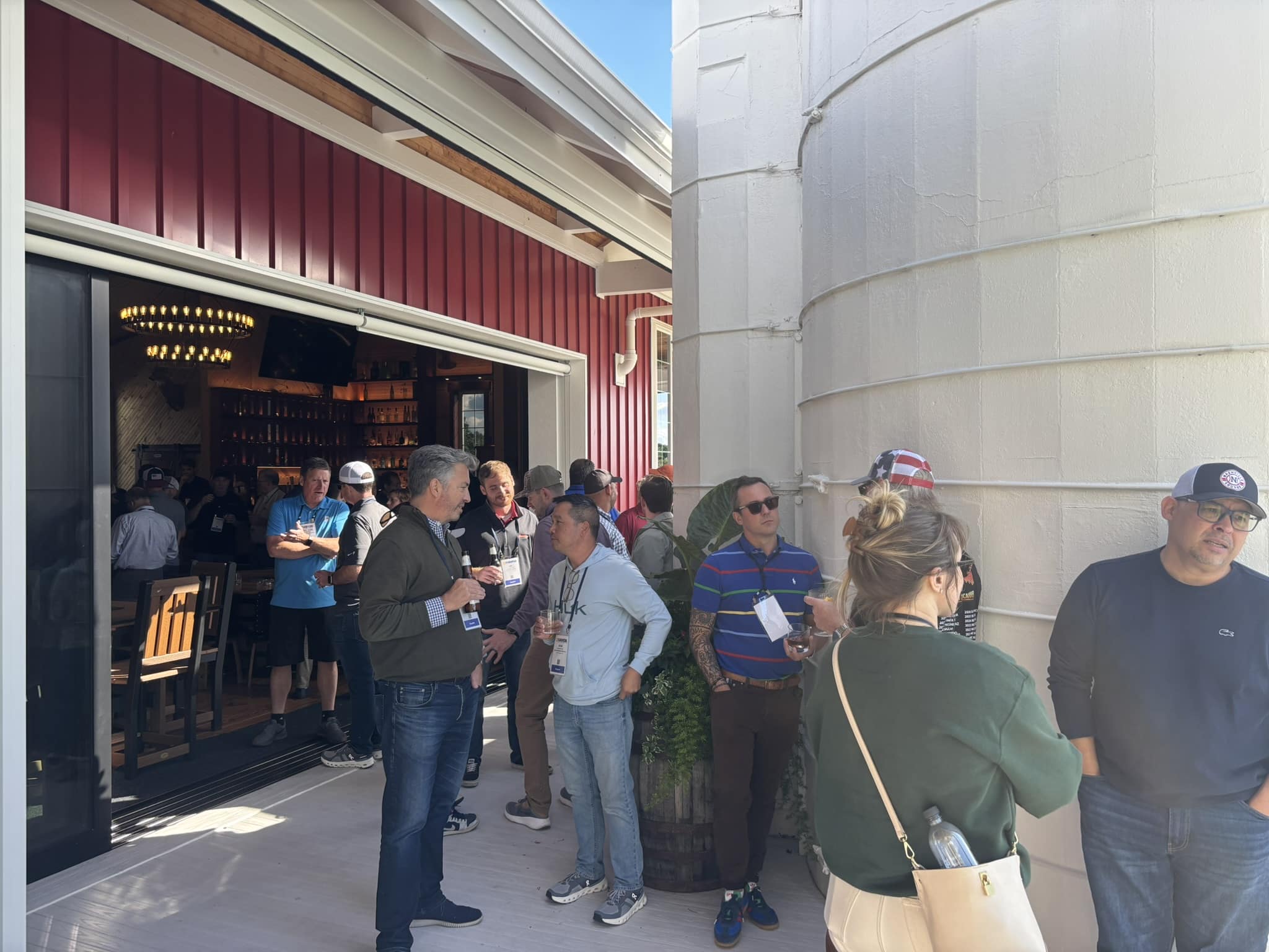 Crowd of people with name badges gathered outside a storefront with red siding and open doorway.