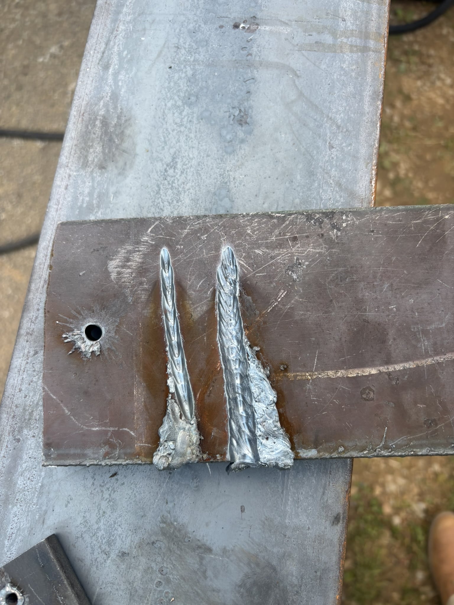 Welded two braided steel rods to a metal plate on a workbench, with a hole and rough metal surface nearby (welding site).