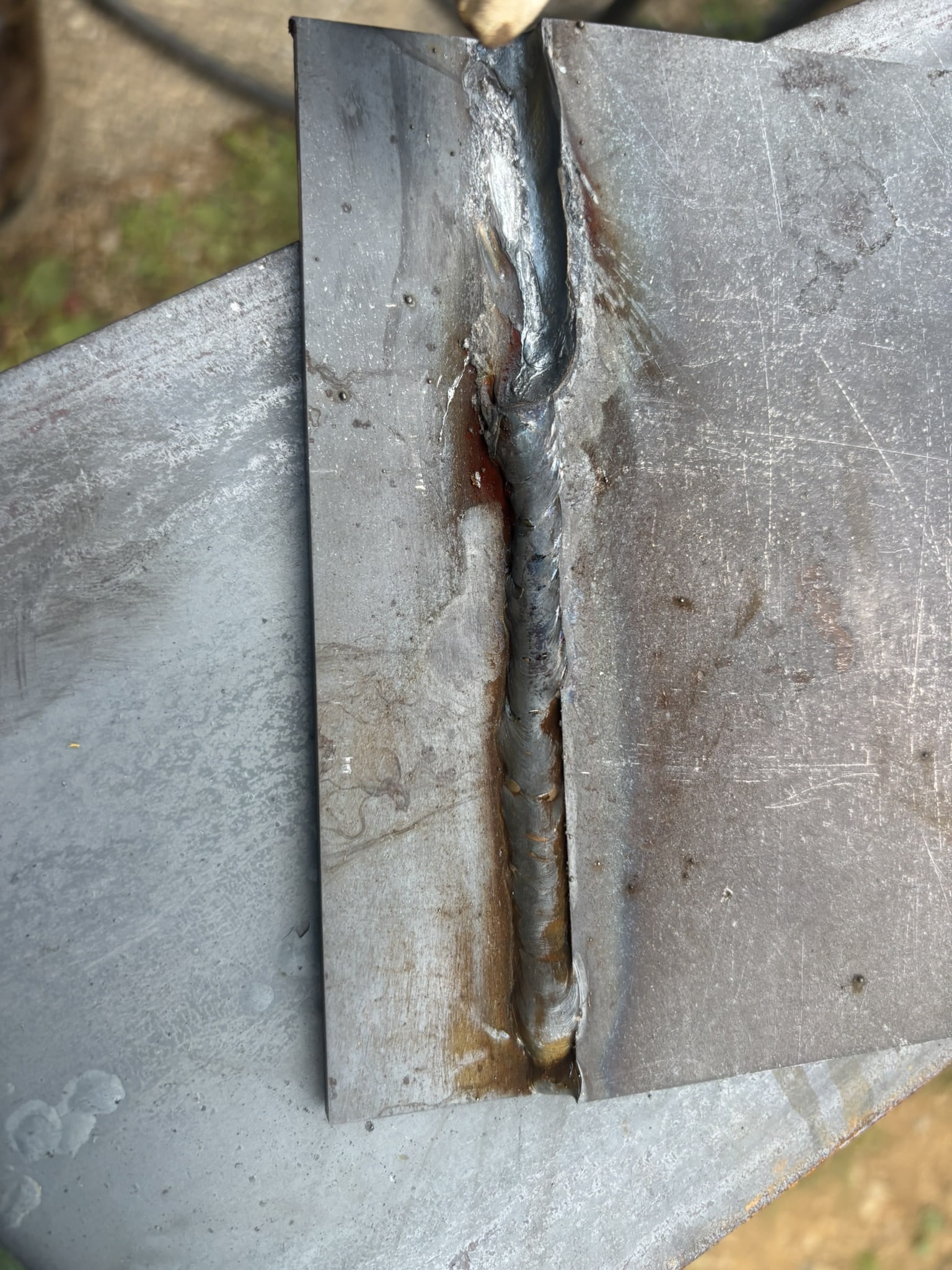 Close-up of a welded joint between two metal plates with rust and heat discoloration; the weld bead runs along the seam.