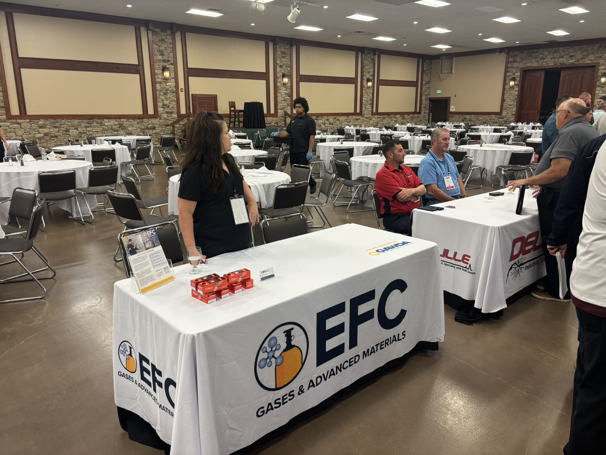 Exhibition booth for EF C Gases  Advanced Materials in a banquet hall, with staff at the table and rows of set tables in the background.