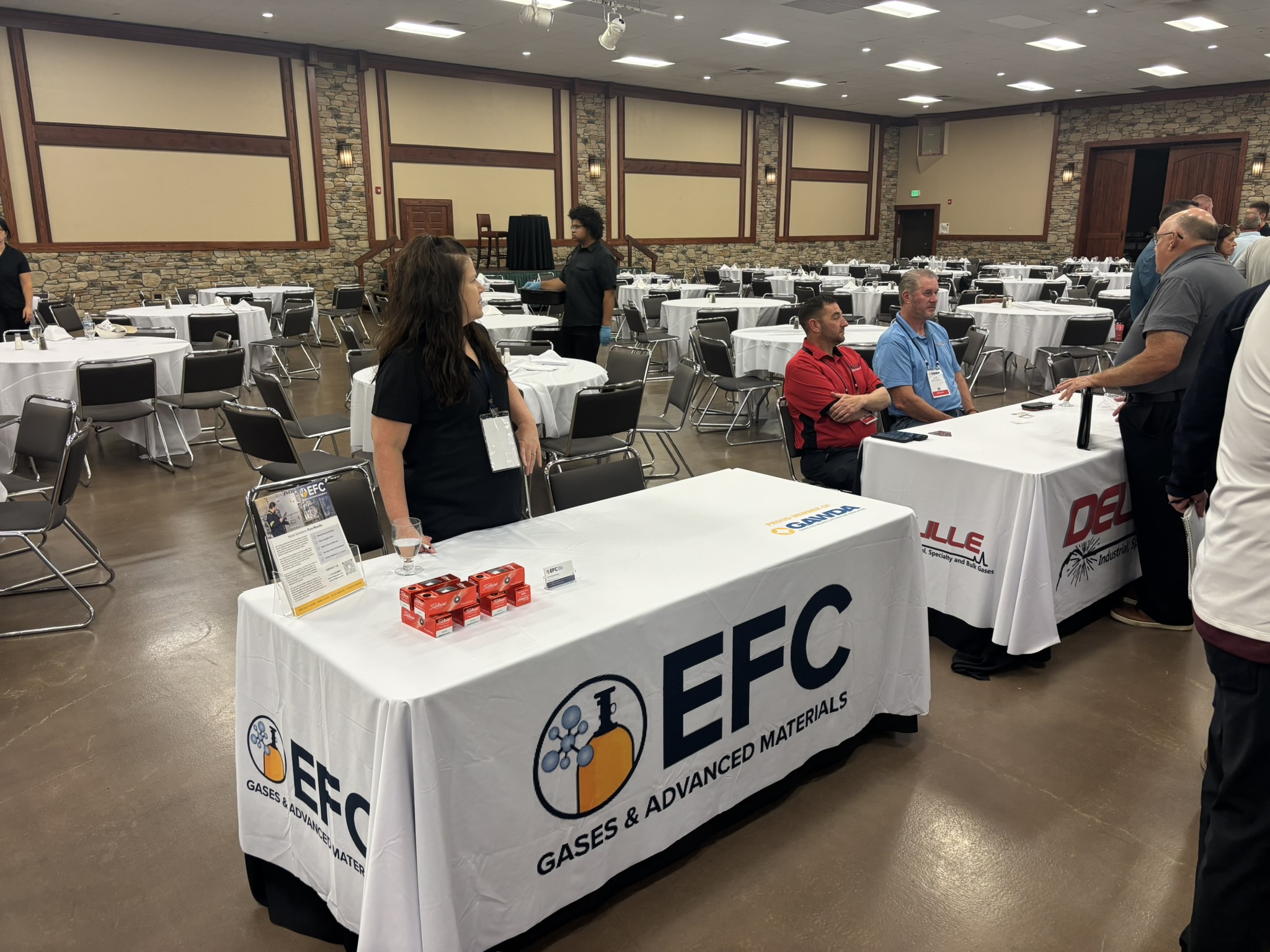 Conference hall set for an event with round tables and EFEC booth banners in the foreground.