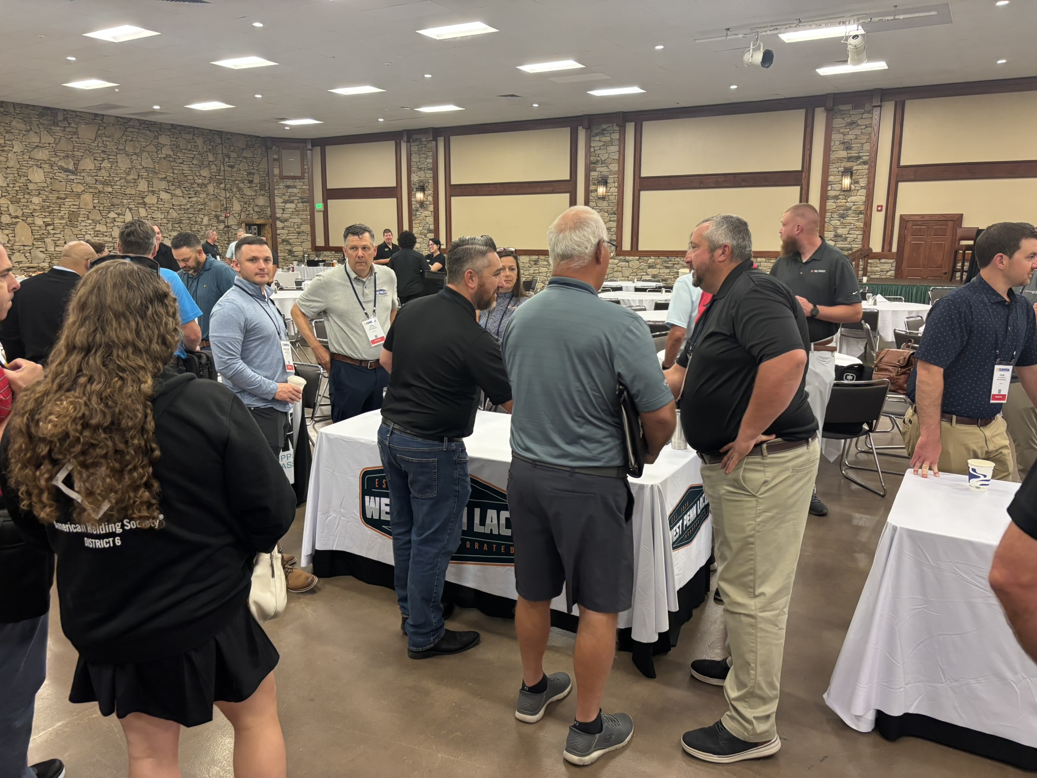 Group of attendees at a conference talking near decorated tables in a banquet hall with stone walls and warm lighting.