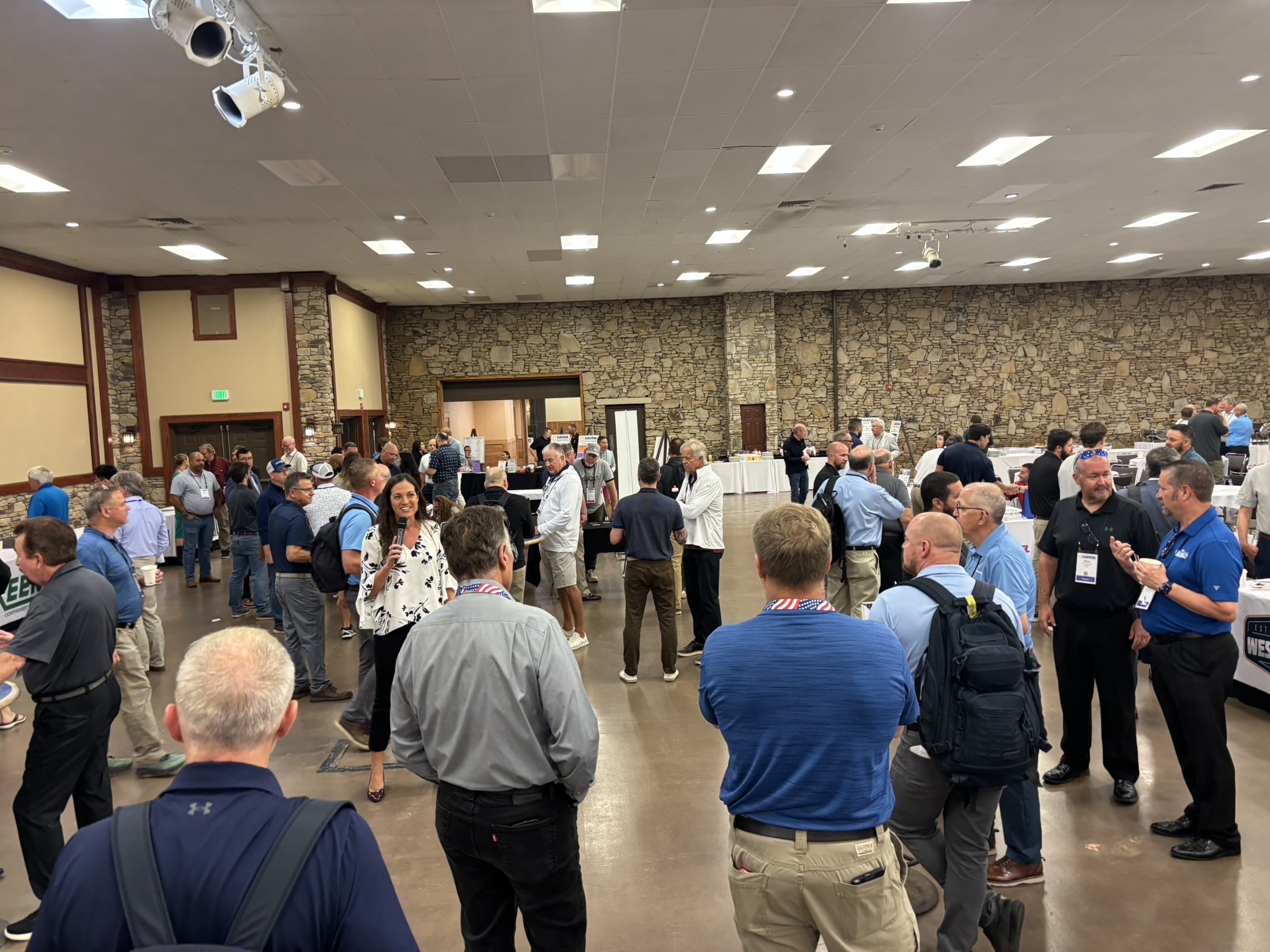 Crowd of people at an indoor conference or expo in a large hall with stone walls and vendor booths in the background.