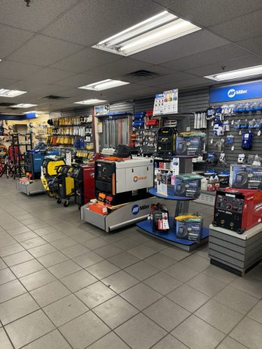 Interior of a hardware store showing tool displays, gloves, and various equipment on pegboard walls under bright fluorescent lights