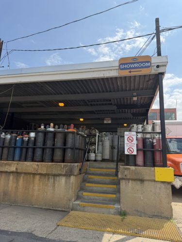 Showroom entrance with gas cylinders lined up outside and a leftward showroom arrow sign above.