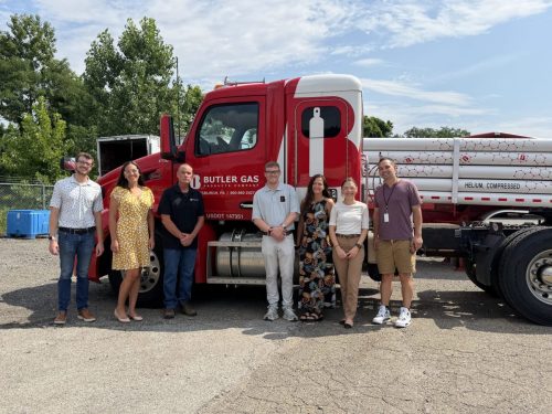 Group of eight people standing in a line in front of a red Butler Gas truck trailer in a parking lot on a sunny day.