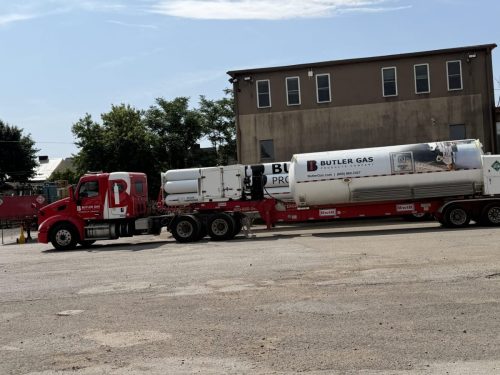 Red Butler Gas tanker truck parked beside a brown two-story building under a clear blue sky.