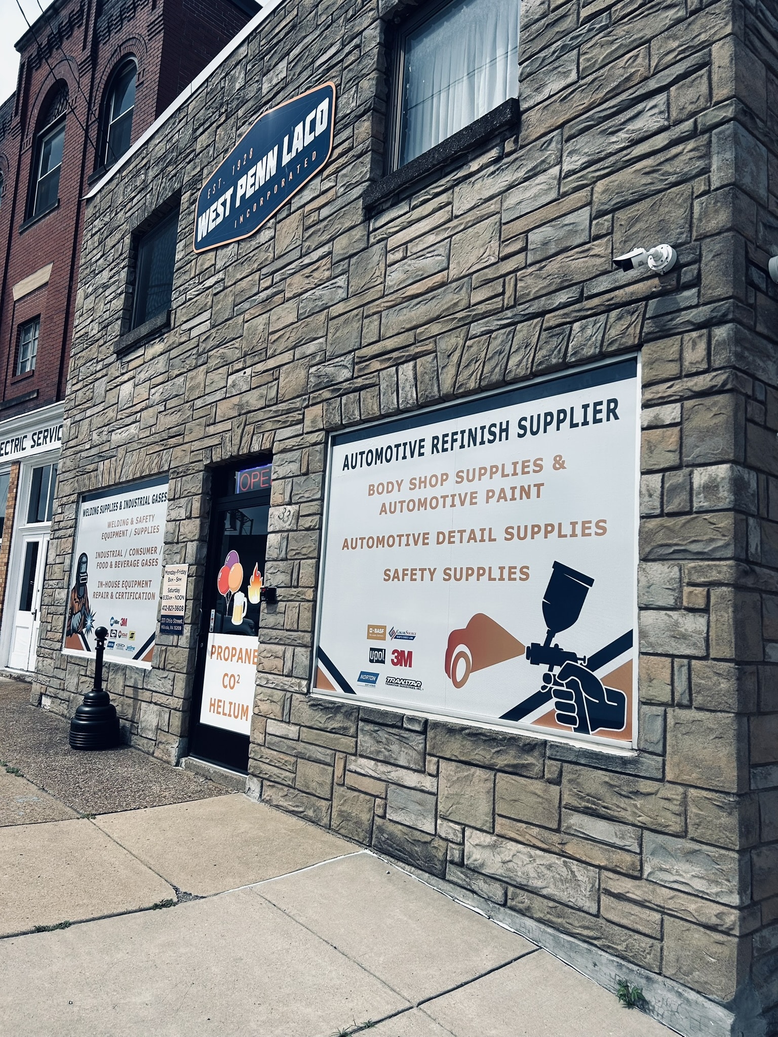 Stone storefront with a large 'Automotive Refinish Supplier' sign in the window and a security camera on the wall.