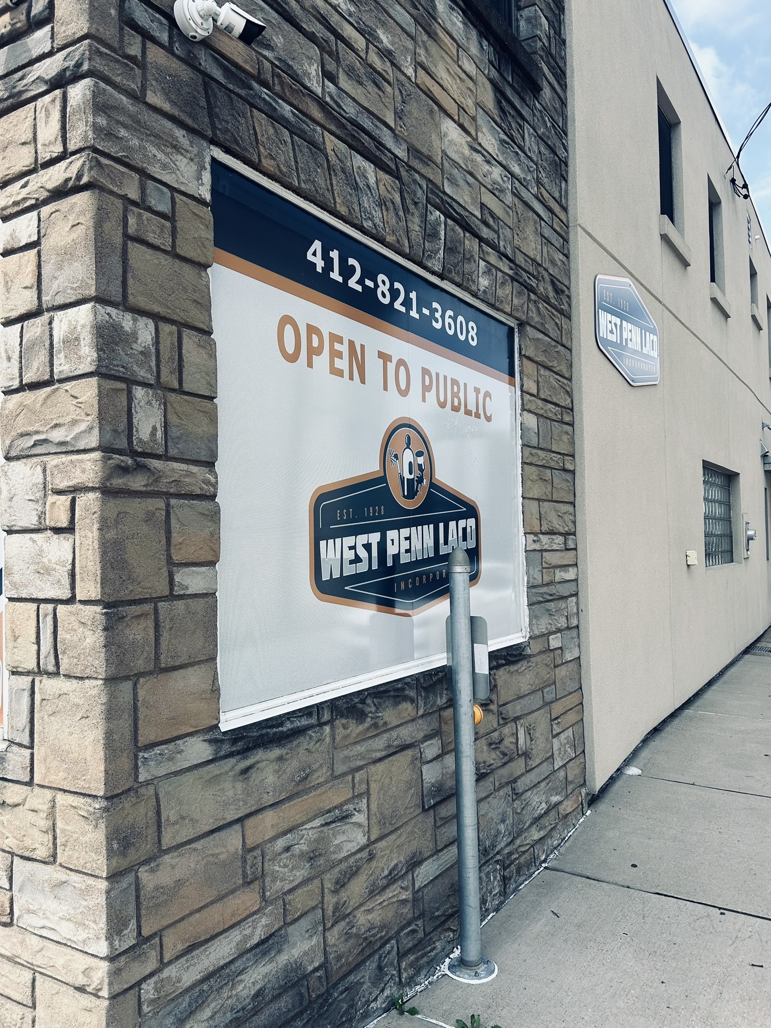 Storefront with a stone brick exterior, a security camera overhead, and a banner reading 'OPEN TO PUBLIC' on the window.