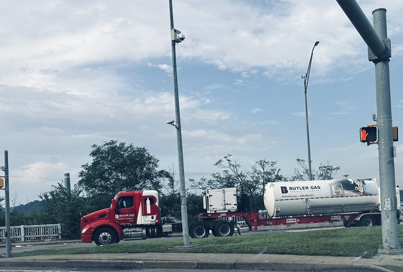 Red semi-truck with a large Butler Gas tanker trailer on a city street at an intersection.